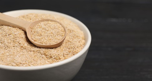 Photo of Oat bran in bowl and spoon on black table, closeup. Space for text