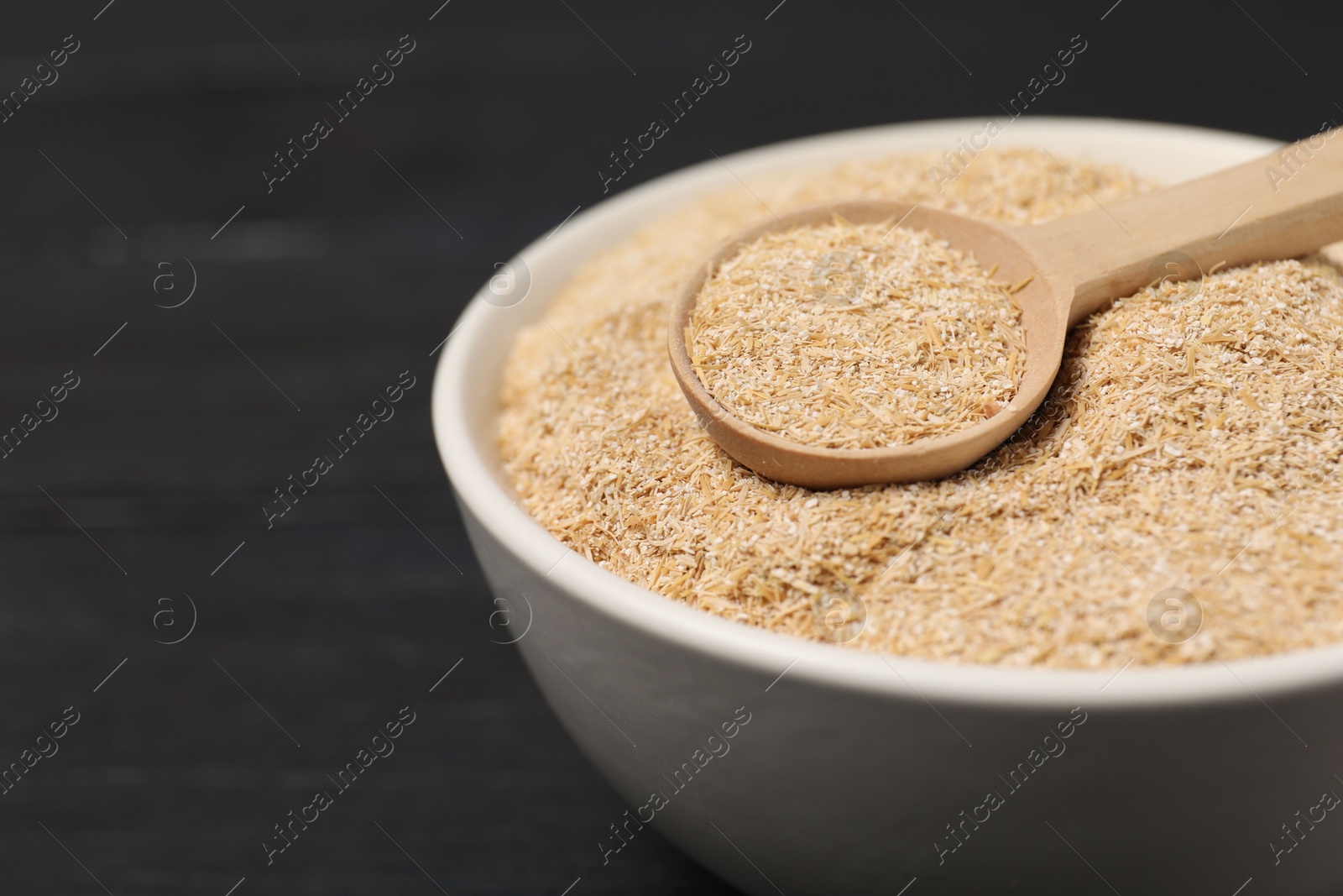 Photo of Oat bran in bowl and spoon on black table, closeup