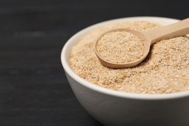 Photo of Oat bran in bowl and spoon on black table, closeup