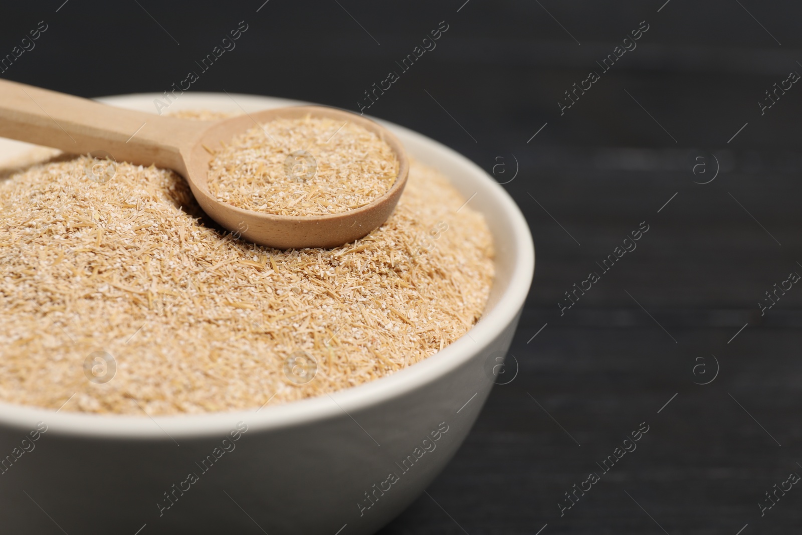 Photo of Oat bran in bowl and spoon on black table, closeup