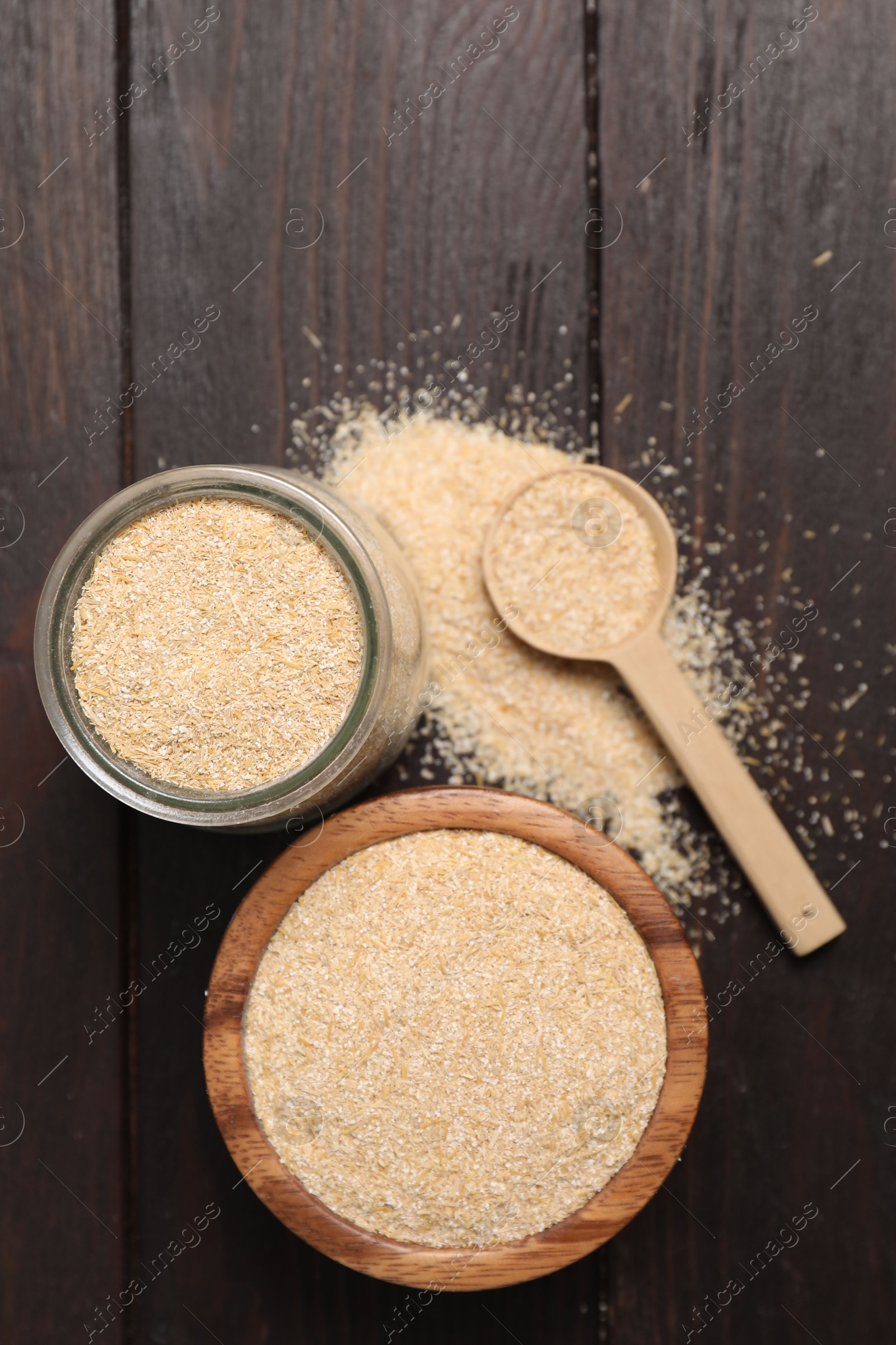 Photo of Oat bran in glass jar, bowl and spoon on wooden table, top view