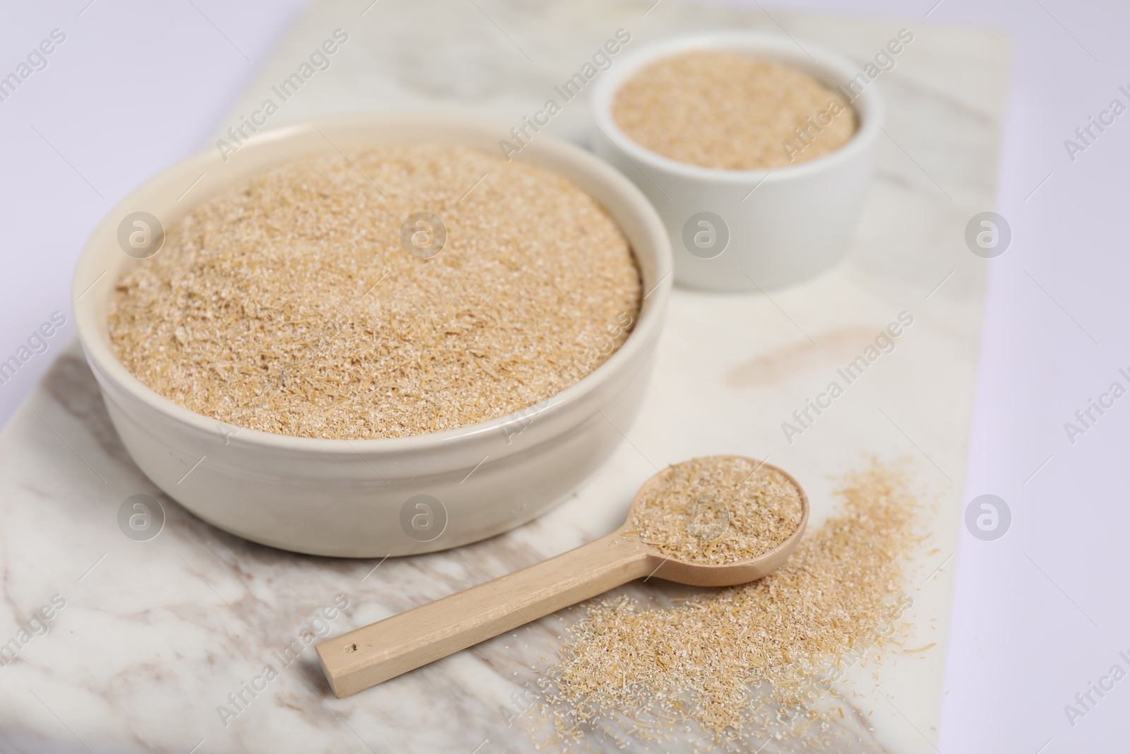 Photo of Oat bran in bowls and spoon on white table, closeup