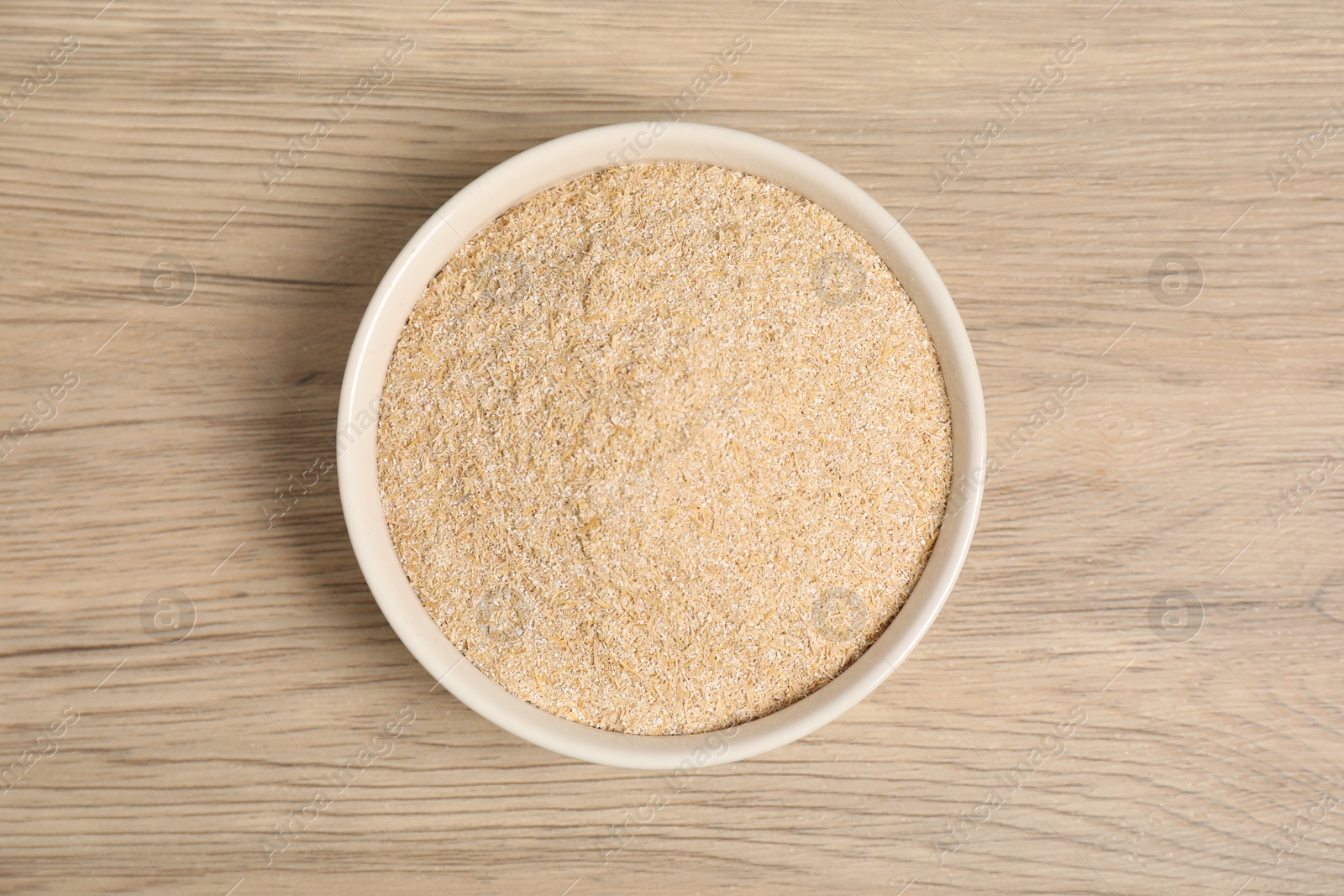 Photo of Oat bran in bowl on wooden table, top view