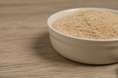 Photo of Oat bran in bowl on wooden table, closeup. Space for text