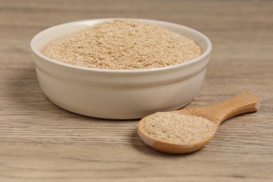 Photo of Oat bran in bowl and spoon on wooden table, closeup