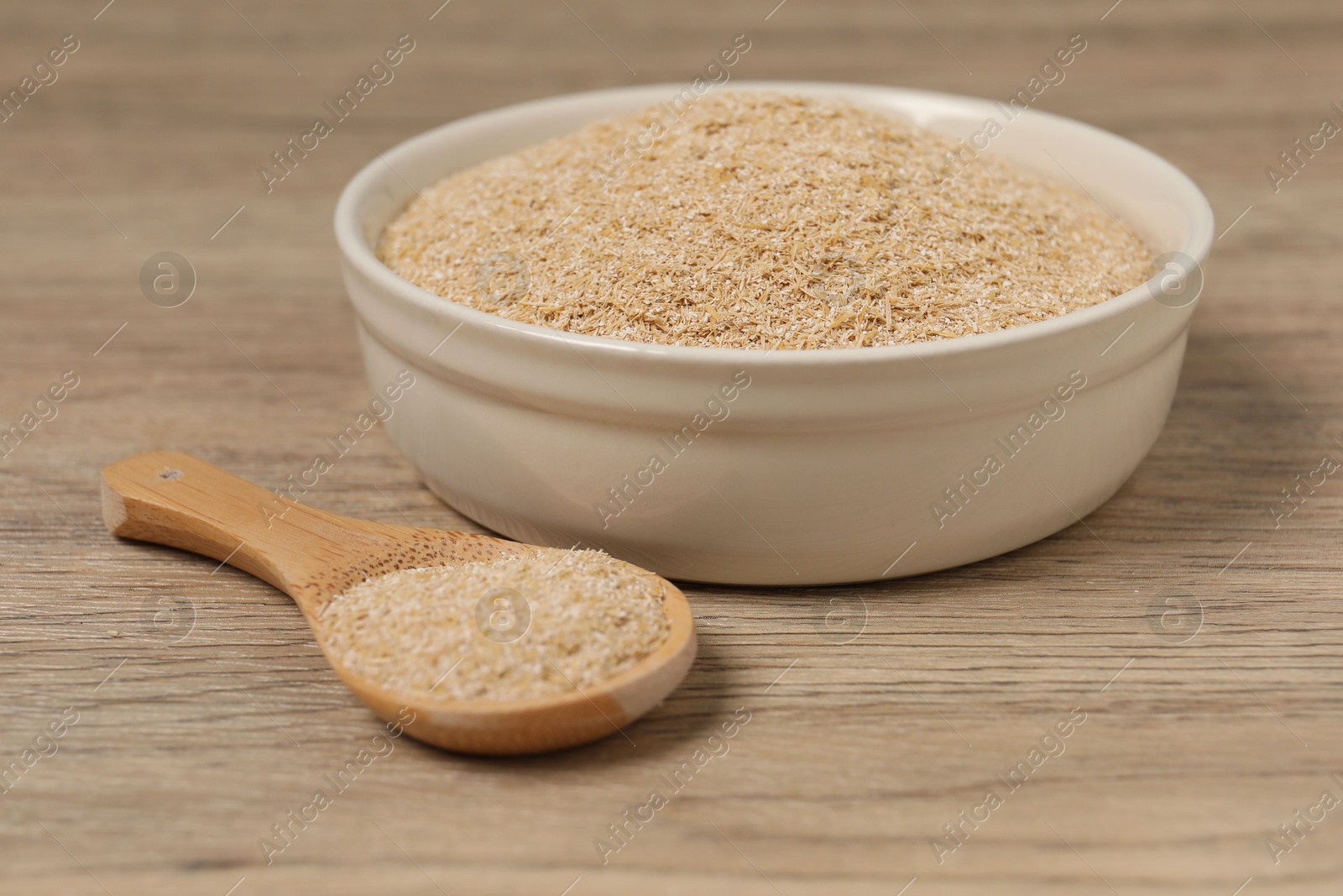 Photo of Oat bran in bowl and spoon on wooden table, closeup