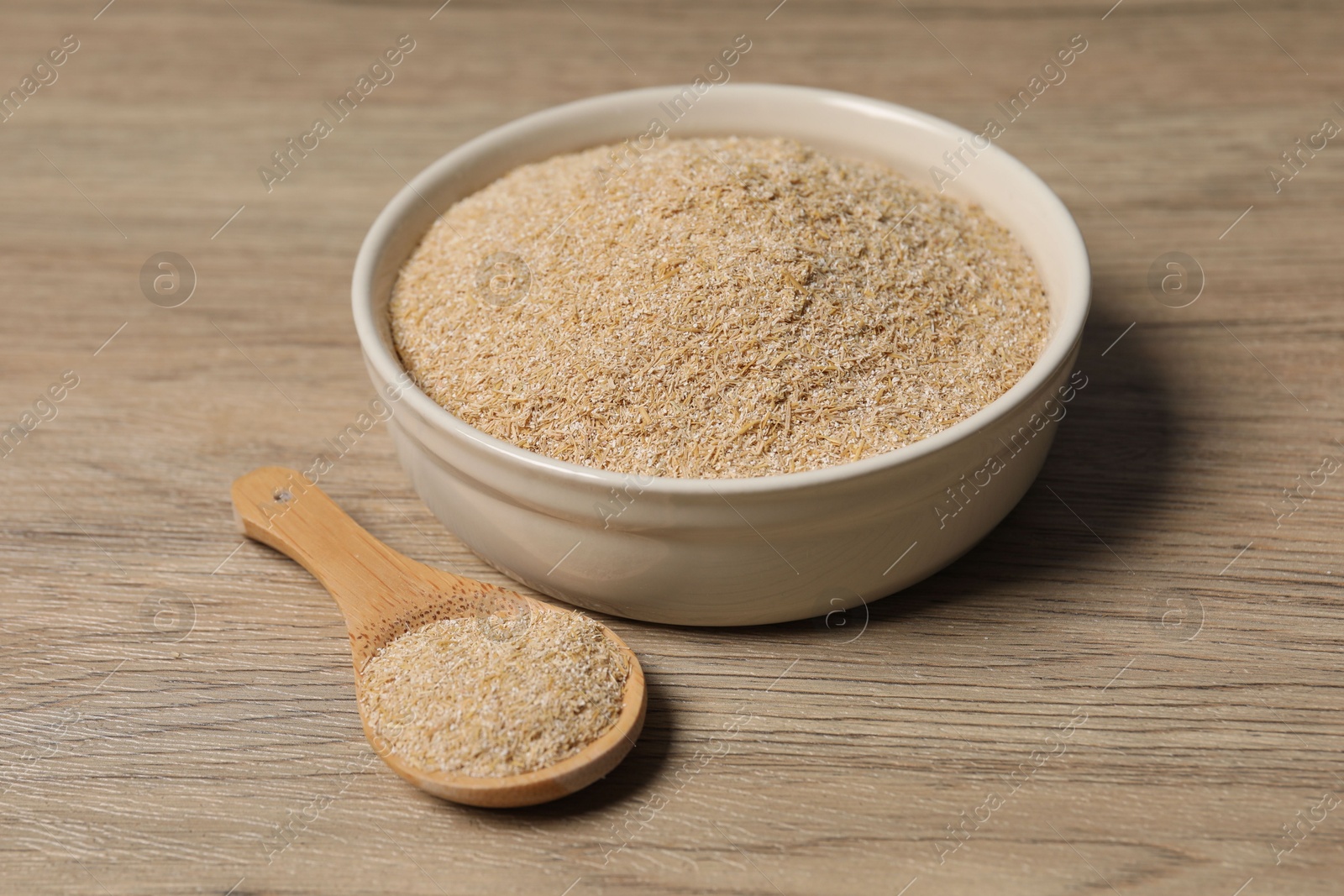 Photo of Oat bran in bowl and spoon on wooden table, closeup