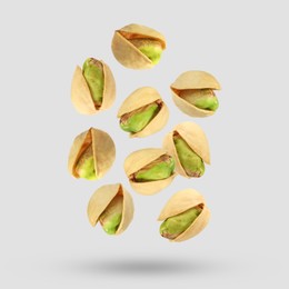 Tasty pistachios falling on light grey background