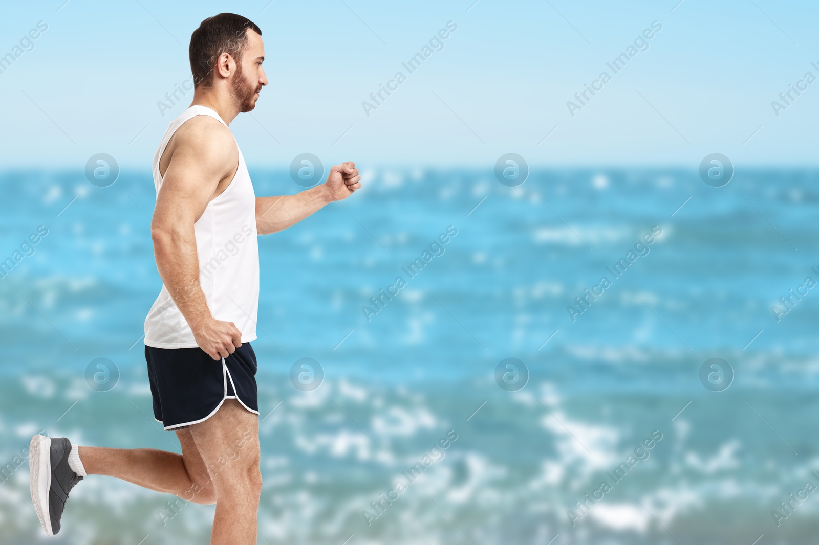 Image of Sporty man running on beach. Space for text