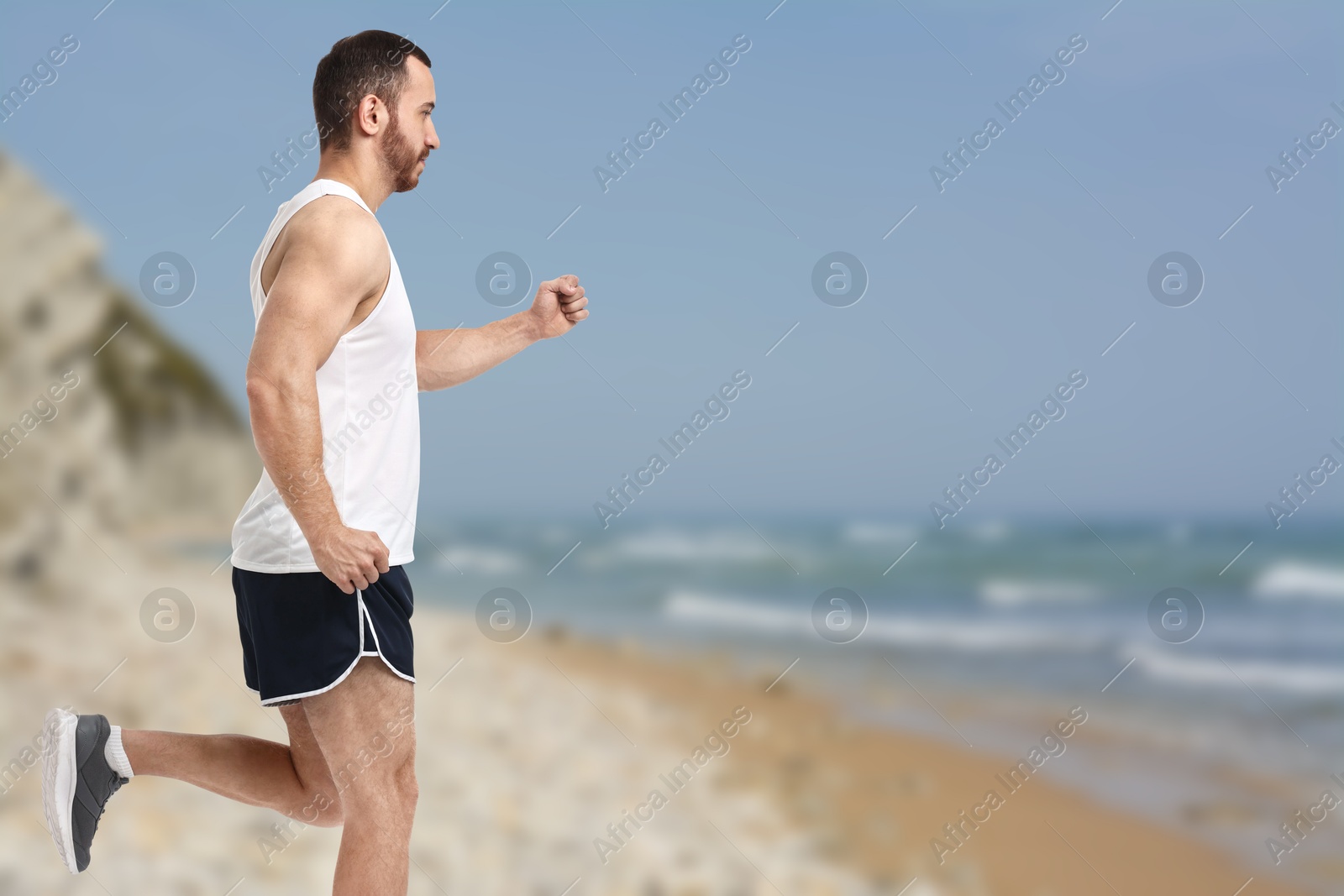 Image of Sporty man running on beach. Space for text