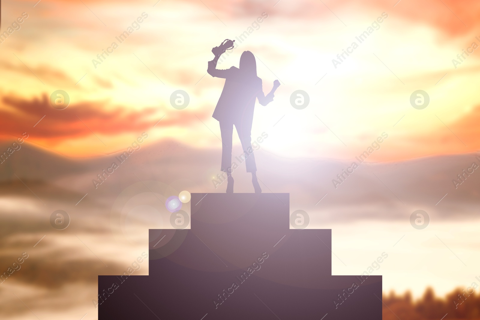 Image of Winner with trophy cup on podium in mountains at sunrise