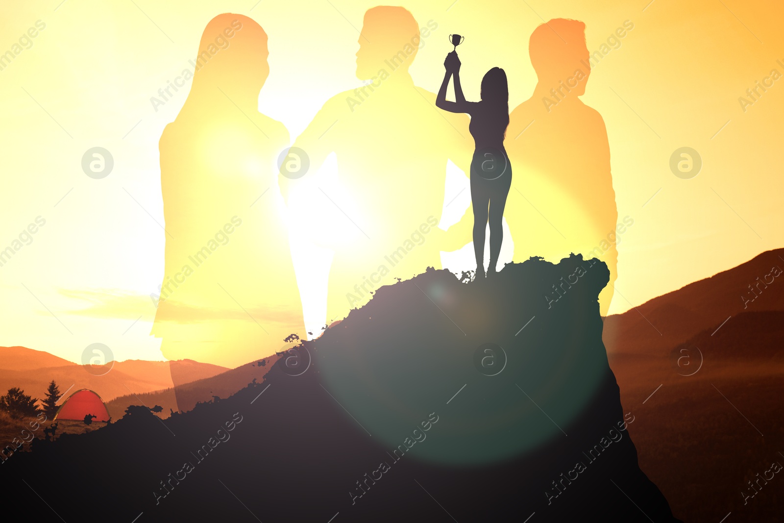 Image of Winner with trophy cup in mountains at sunrise and silhouettes of people