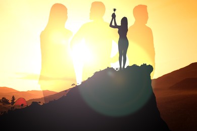 Winner with trophy cup in mountains at sunrise and silhouettes of people