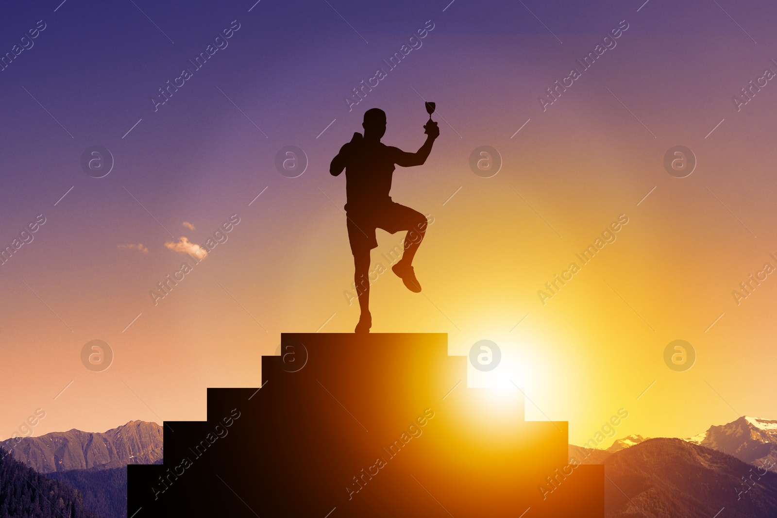 Image of Winner with trophy cup on podium in mountains at sunrise