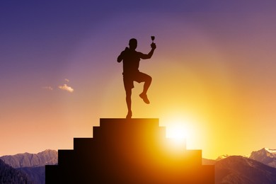 Winner with trophy cup on podium in mountains at sunrise