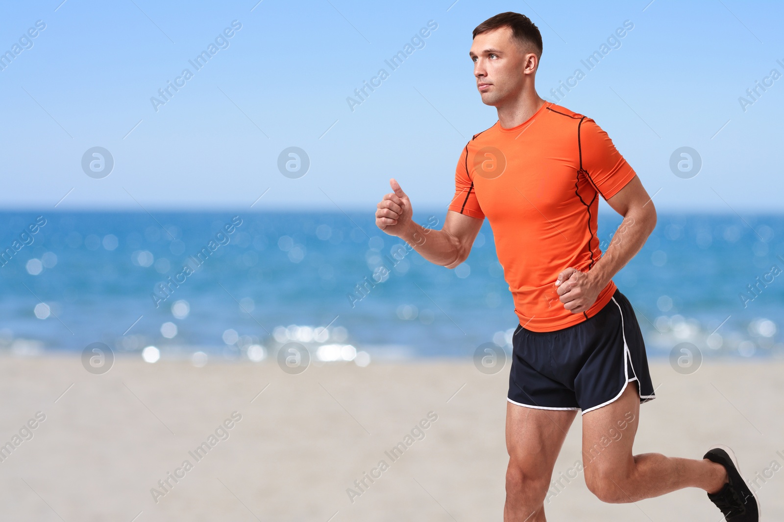 Image of Sporty man running on beach. Space for text