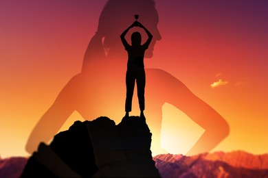 Winner with trophy cup in mountains at sunrise and silhouette of woman