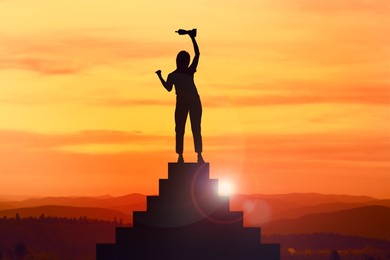 Winner with trophy cup on podium in mountains at sunrise