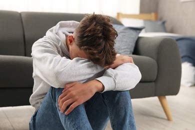 Photo of Loneliness concept. Sad teenage boy on floor at home