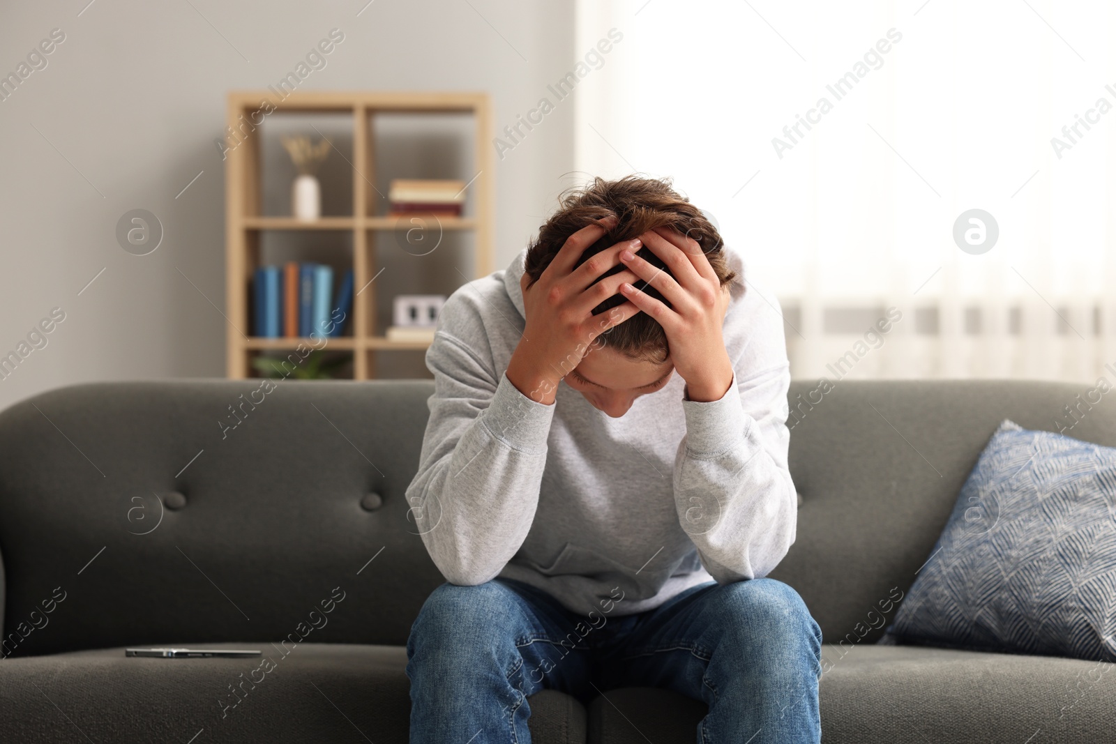 Photo of Loneliness concept. Sad teenage boy with smartphone on sofa at home