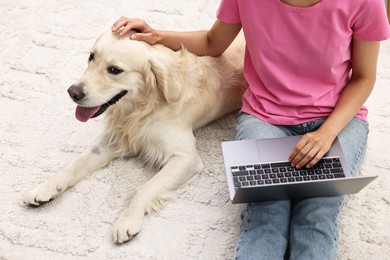 Photo of Online pet shop. Woman with laptop making order for cute Golden Retriever dog on rug at home, closeup