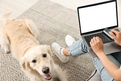 Photo of Online pet shop. Woman with laptop, credit card and cute Golden Retriever dog making order at home, closeup