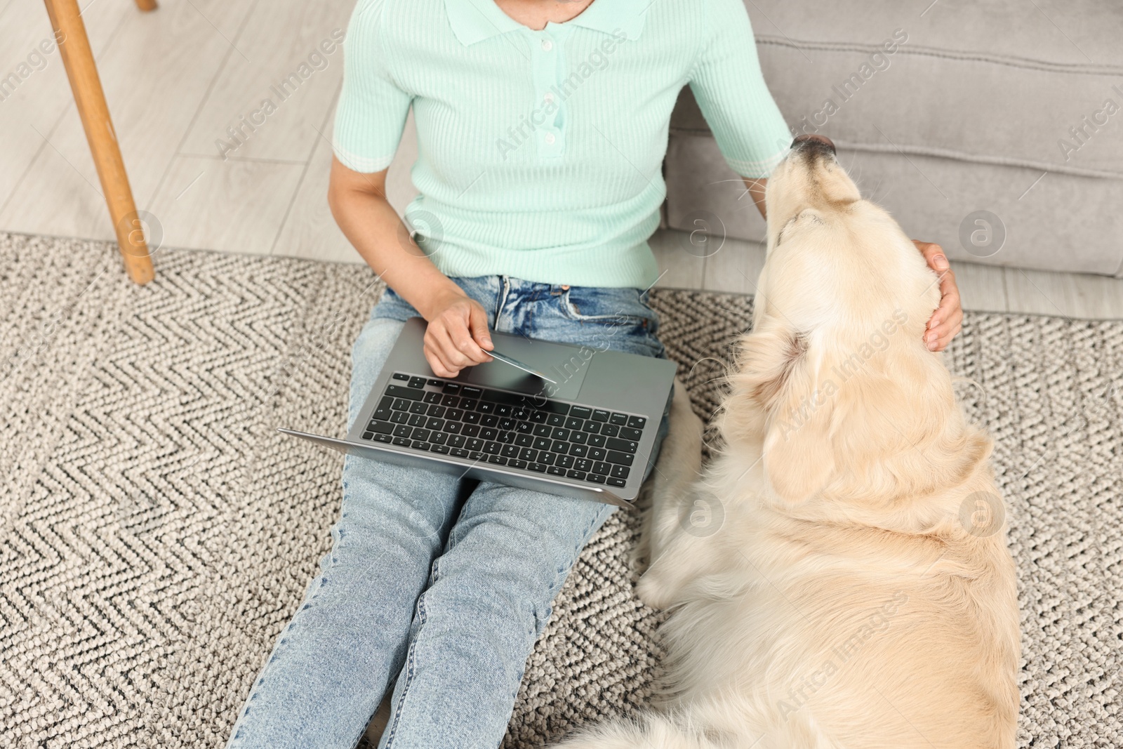 Photo of Online pet shop. Woman with laptop, credit card and cute Golden Retriever dog making order at home, closeup