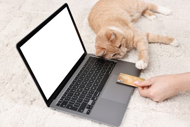 Online pet shop. Woman with laptop, credit card and cute cat making order on rug at home, closeup