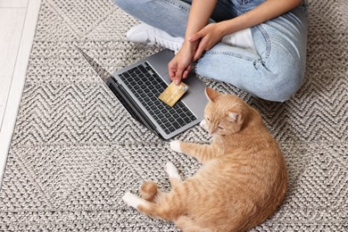 Photo of Online pet shop. Woman with laptop, credit card and cute cat making order on rug at home, closeup