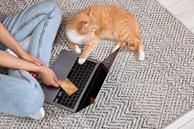 Online pet shop. Woman with laptop, credit card and cute cat making order on rug at home, closeup