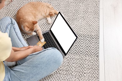 Photo of Online pet shop. Woman with laptop, credit card and cute cat making order on rug at home, closeup