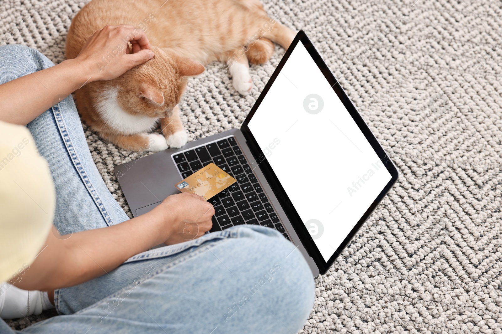 Photo of Online pet shop. Woman with laptop, credit card and cute cat making order on rug at home, closeup