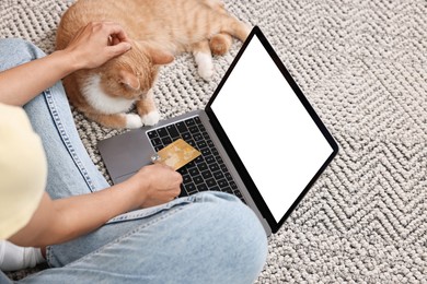 Online pet shop. Woman with laptop, credit card and cute cat making order on rug at home, closeup