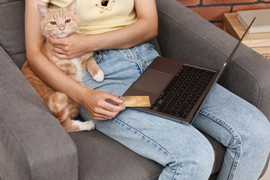 Photo of Online pet shop. Woman with laptop, credit card and cute cat making order on armchair at home, closeup