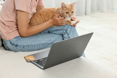 Online pet shop. Woman with laptop, credit card and cute cat making order on sofa at home, closeup