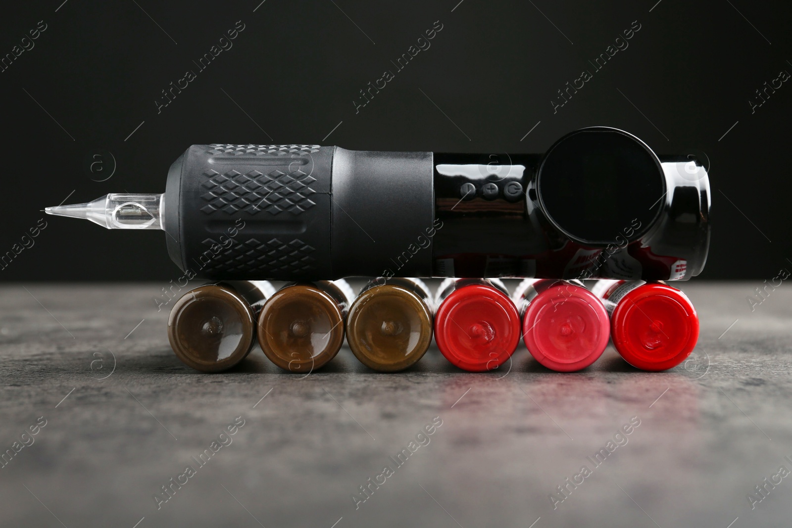 Photo of Professional permanent makeup machine and bottles of pigments on grey table