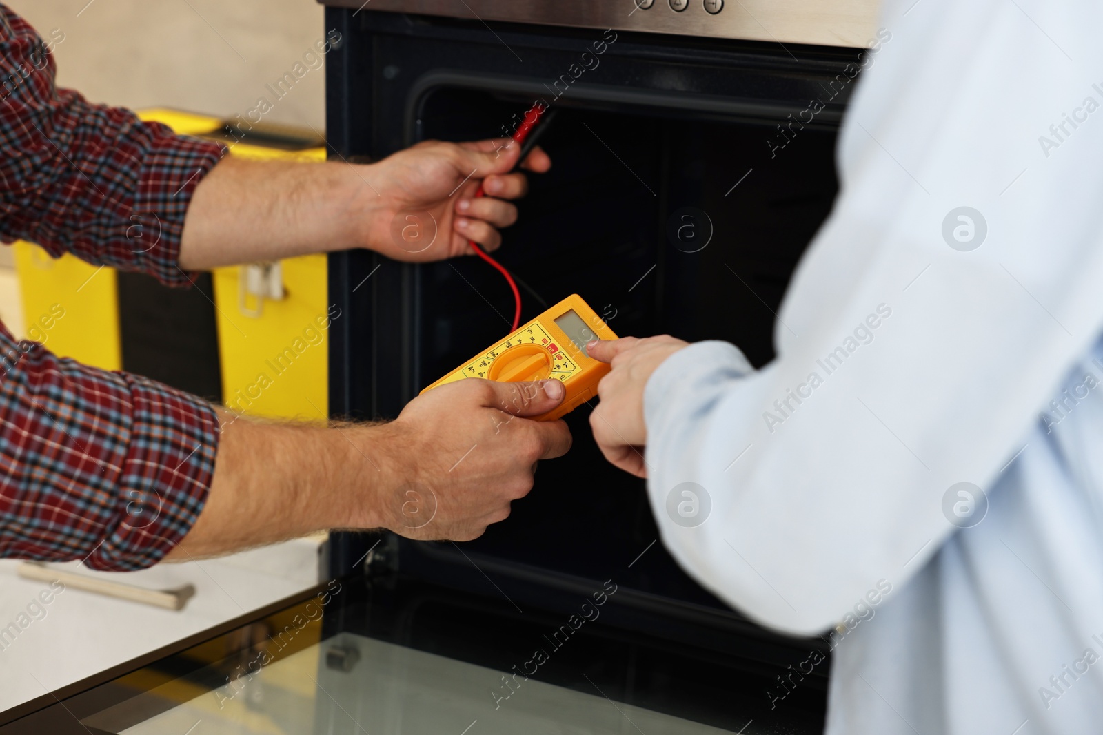 Photo of Repairman and woman testing oven element with multimeter, closeup