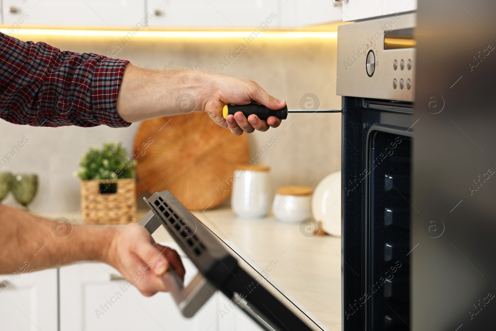 Photo of Repairman with screwdriver fixing oven in kitchen, closeup