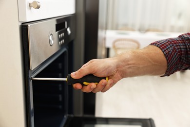 Photo of Repairman with screwdriver fixing oven indoors, closeup