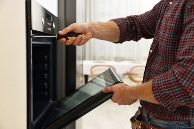 Photo of Repairman with screwdriver fixing oven indoors, closeup