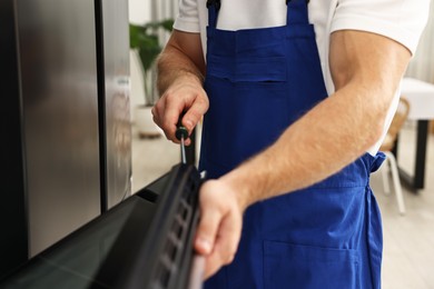 Photo of Repairman with screwdriver fixing oven indoors, closeup