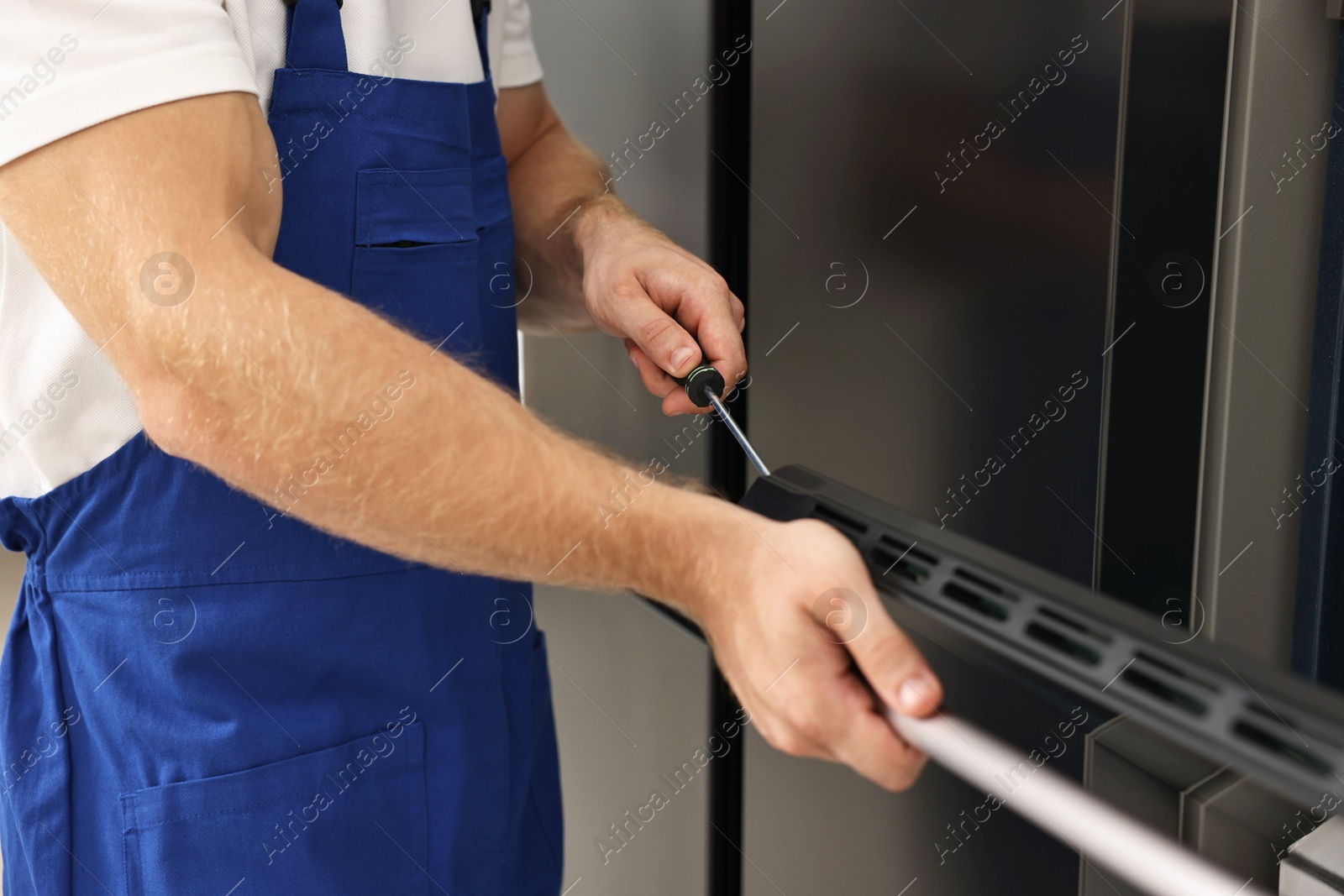 Photo of Repairman with screwdriver fixing oven indoors, closeup