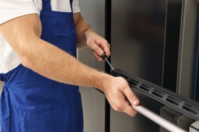 Photo of Repairman with screwdriver fixing oven indoors, closeup