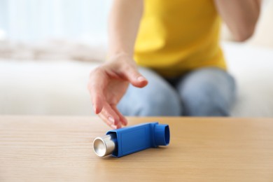 Young woman using asthma inhaler at home, selective focus