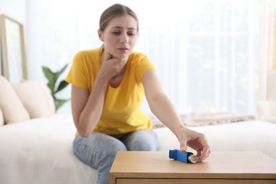 Young woman using asthma inhaler at home, selective focus