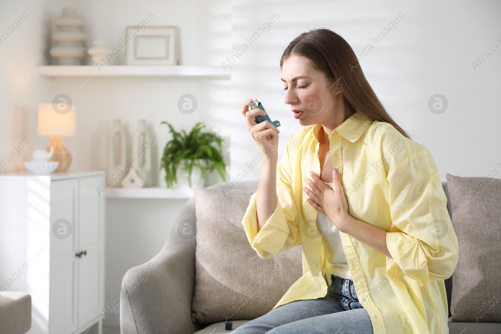 Photo of Young woman using asthma inhaler at home. Space for text