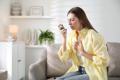 Young woman using asthma inhaler at home. Space for text