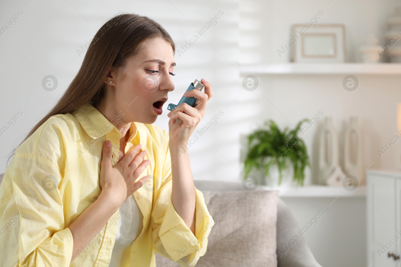 Photo of Young woman using asthma inhaler at home. Space for text