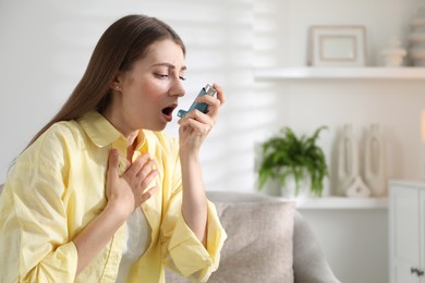 Young woman using asthma inhaler at home. Space for text