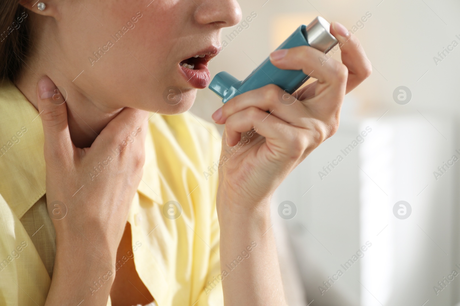 Photo of Young woman using asthma inhaler at home, closeup